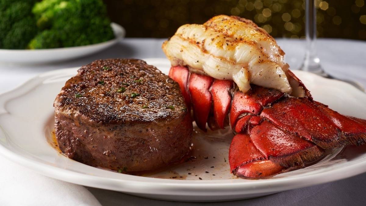 Steak and lobster on a white place with a plate of broccoli in the background